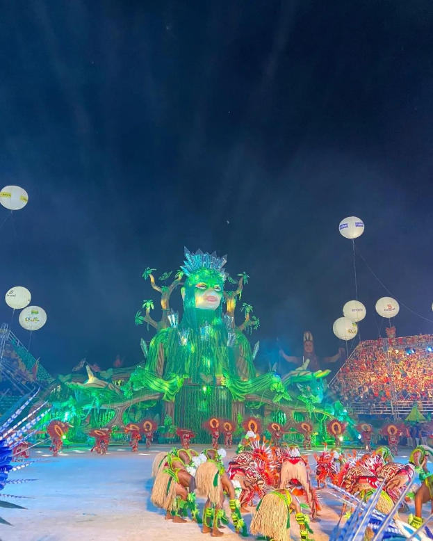 Ein farbenfroher Karneval in Rio de Janeiro, Brasilien, mit Menschen in bunten Kostümen auf der Bühne, einer großen Menge im Publikum und einem Himmel voller bunter Lichter und Ballons.