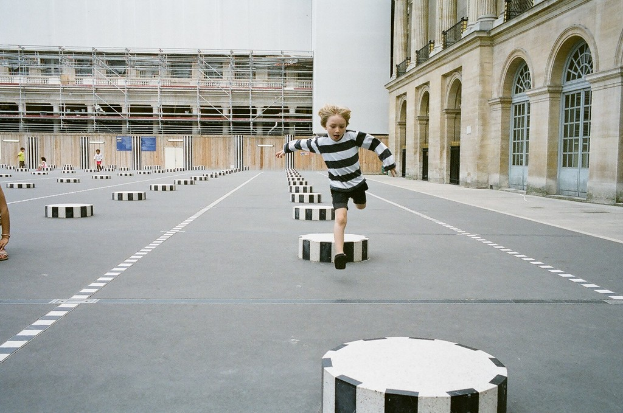 Vier Kinder sind in einem Schulhof mit schwarzen und weißen Betonstufen, ein Kind läuft auf dem Boden.