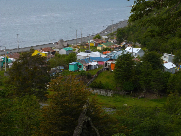 Ein Blick auf Häuser, eine Straße, Pfähle, einen Zaun, Bäume, Gras und einen Wasserlauf.