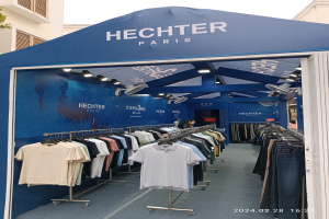 Ein Hechter Paris Stand auf der Paris Fashion Week, mit ausgestellter Kleidung, einer Person, Lichtern, einem Gebäude, einem Baum und einem sichtbaren Himmel, mit einem Wasserzeichen in der rechten unteren Ecke.