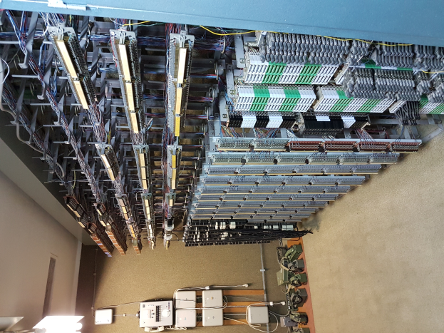 Ein großer Raum voller Numerous Drähte und elektronischer Geräte auf dem Boden, mit einer Wand auf der linken Seite, ähnlich einem Datenzentrum mit verschiedenen Servern und miteinander verbundenen Kabeln.