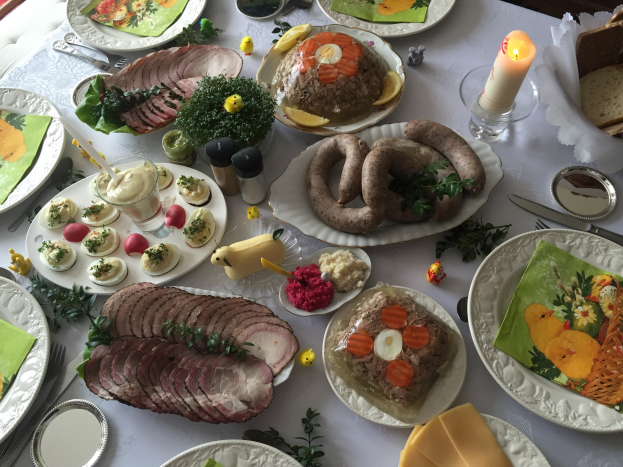Ein Tisch mit verschiedenen Speisen, Tellern, Schüsseln, Besteck, Gläsern und Kerzen, umgeben von Stühlen, repräsentiert ein traditionelles deutsches Osteressen.