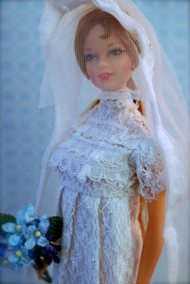 Eine Puppe in einem Kleid, Schleier und mit einem Bukett, vor einem Hintergrundobjekt.