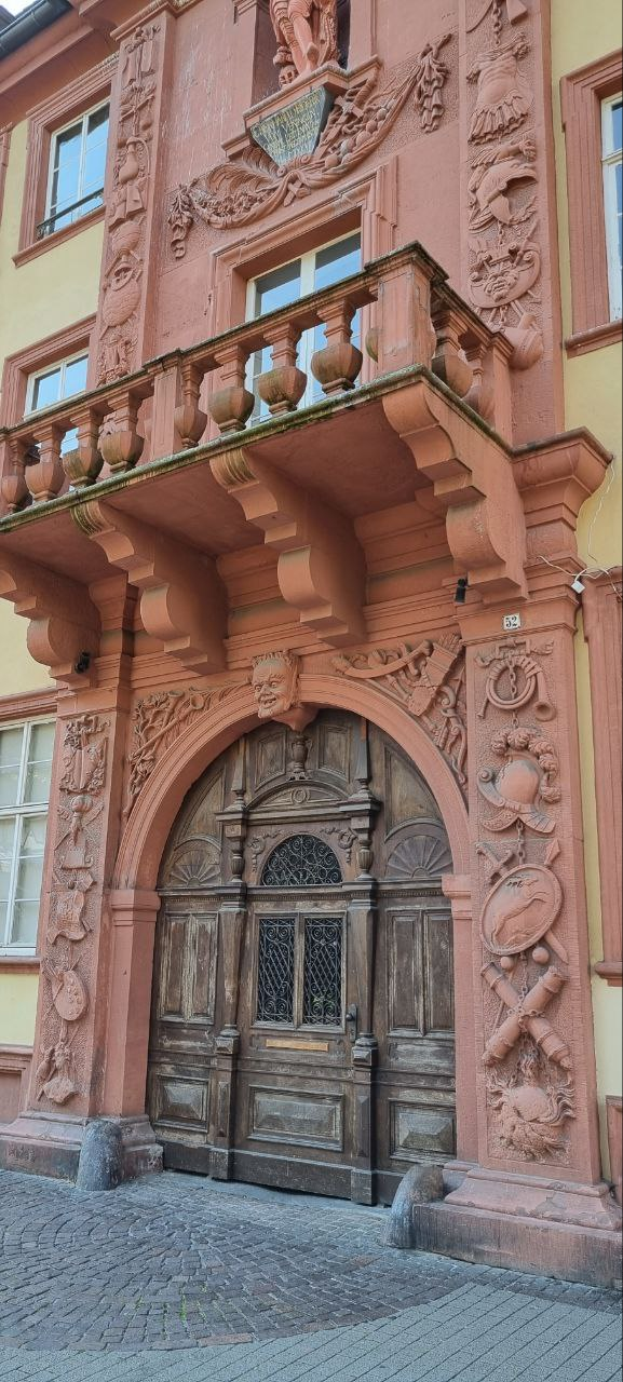 Ein altes Gebäude in Heidelberg, Deutschland, mit einer hölzernen Tür, Fenstern und detaillierten Schnitzereien an der Fassade.