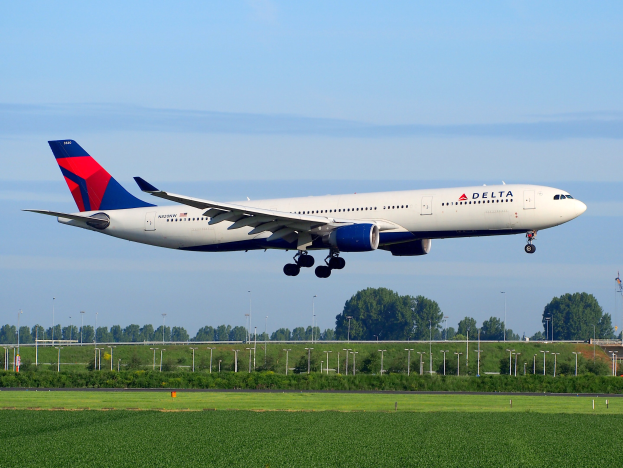 Ein Delta Air Lines Boeing 787-9 Dreamliner startet vom Frankfurter Flughafen, mit grünem Gras, Laternenmasten, Bäumen, einem Turm auf der rechten Seite und weißen Wolken am Himmel.