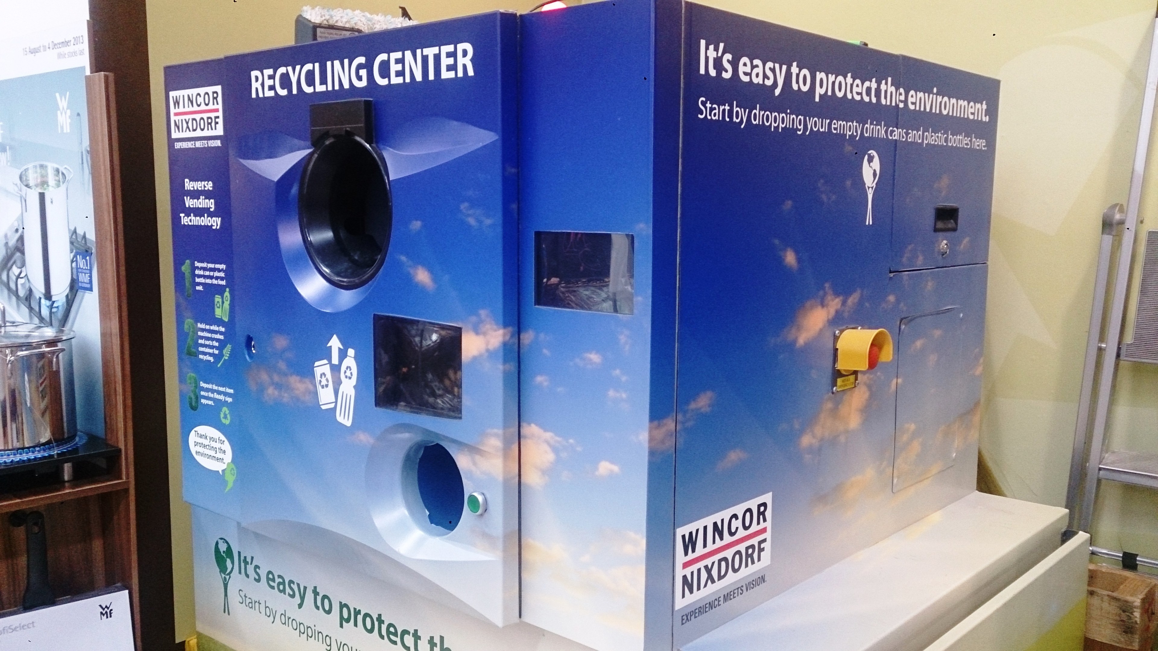 Blaues Recycling-Zentrum mit einem "Recycling-Zentrum"-Schild in der Mitte, einem Gestell mit Gegenständen links, einem einzelnen Gegenstand auf dem Boden rechts und Hintergrundbeleuchtung und Wand.