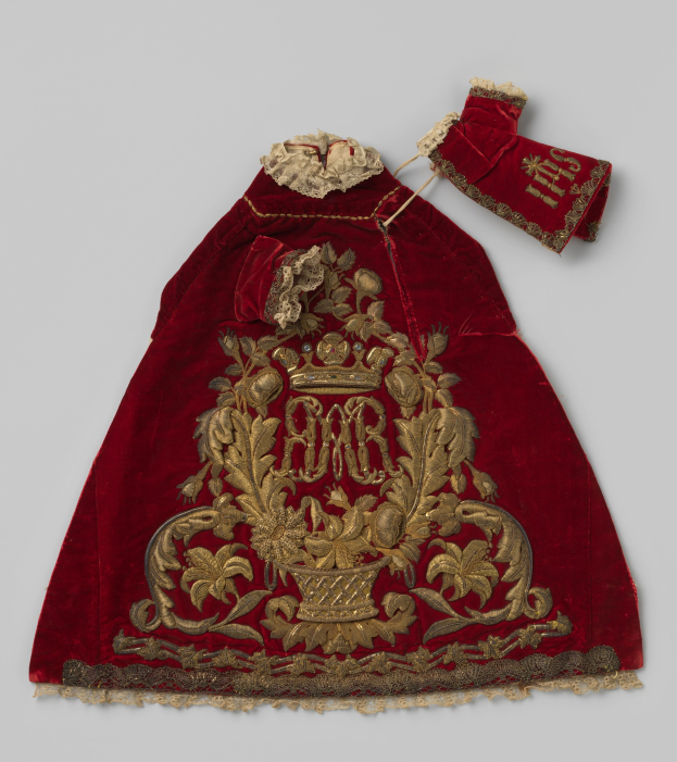 Ein roter Samtmantel mit goldener Stickerei und einer Krone, vor einem weißen Hintergrund.