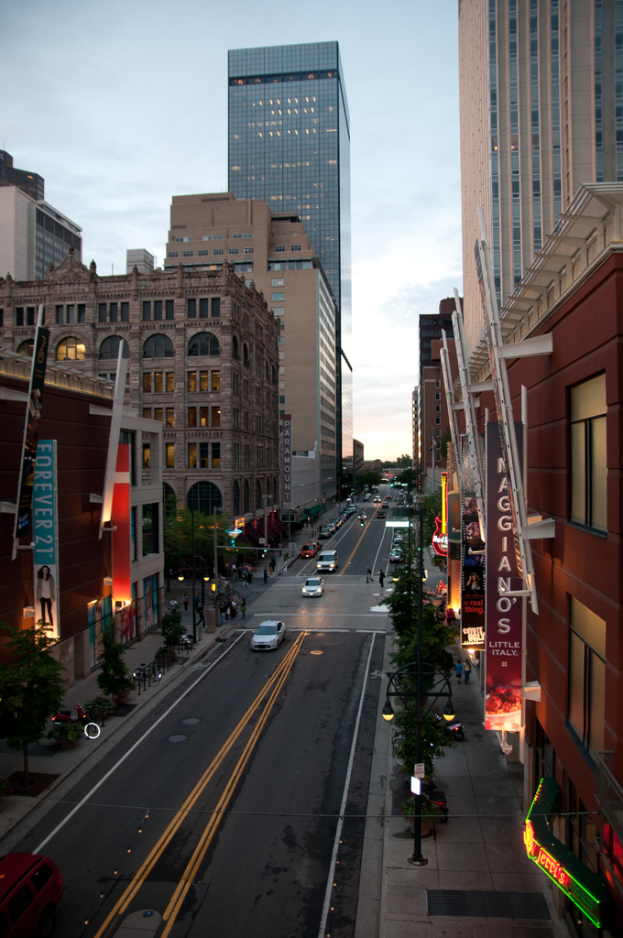 Eine Stadtansicht mit einer Straße, die von Gebäuden und Wolkenkratzern gesäumt ist, unter einem Himmel.