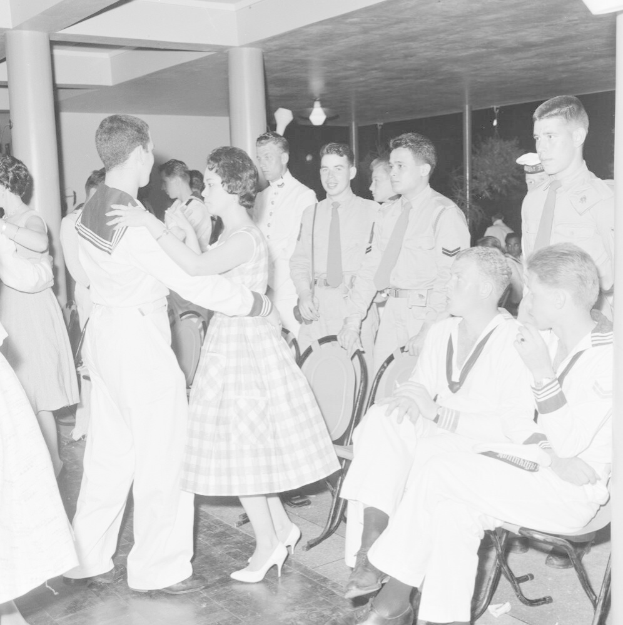 Schwarzes und weißes Bild von Militärpersonal, das tanzt und sich vergnügt in einem dekorierten Saal mit Säulen und Beleuchtung.