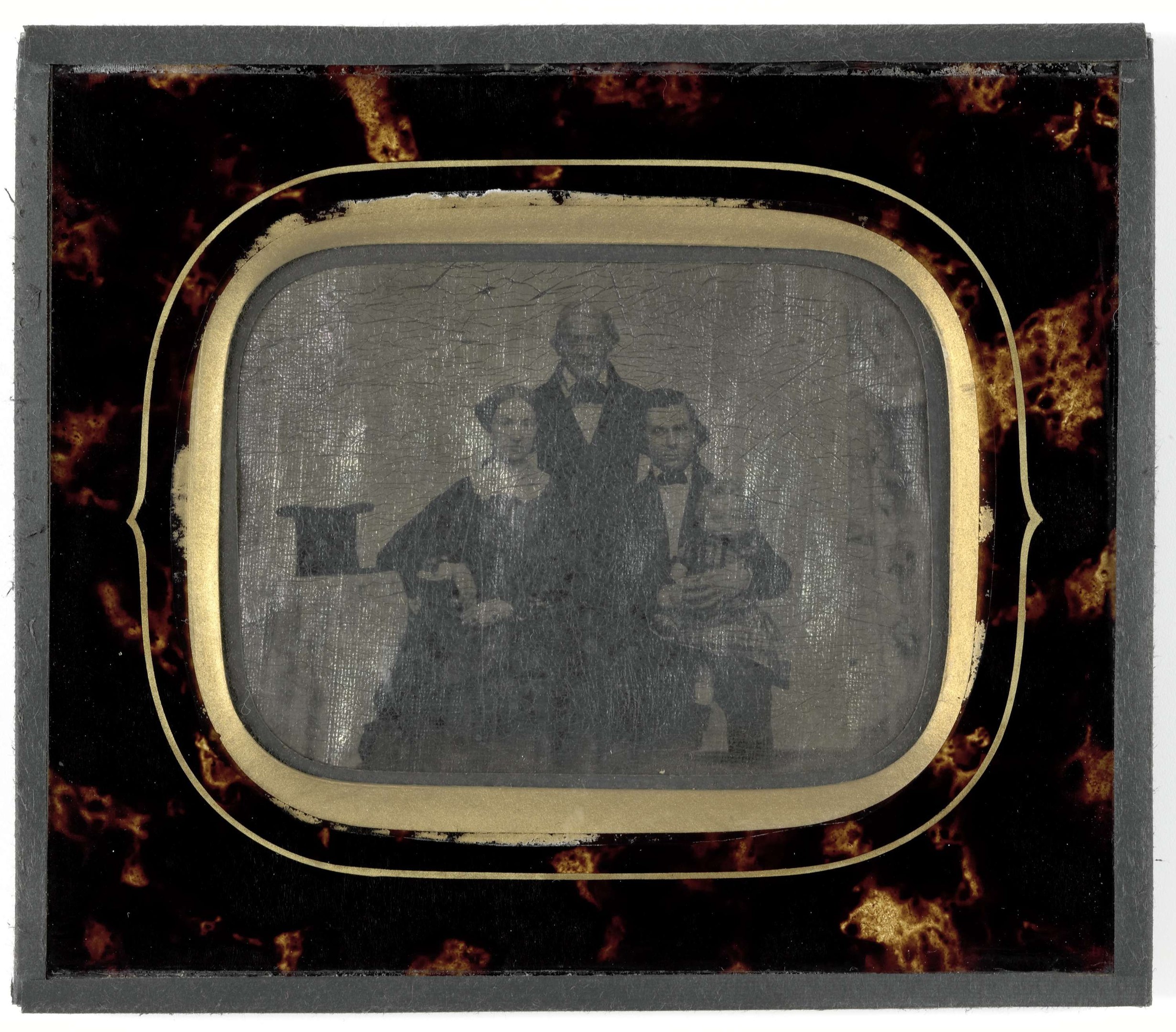 Schwarzes-Weiß-Foto eines Mannes in Anzug und Krawatte und einer Frau in einem unbekannten Outfit, die vor einem alten Fernseher stehen, beide mit ernsten Gesichtern.