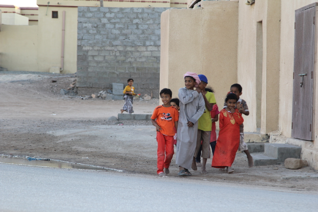 Eine Gruppe strahlender Kinder vor Gebäuden, Wasser, Felsen und einer Straße stehend