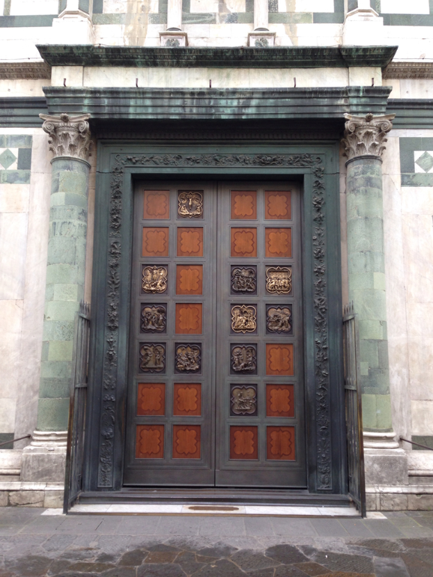 Eine Tür mit Skulpturen darauf, die in eine Wand eingesetzt ist, mit einem Gehweg davor.