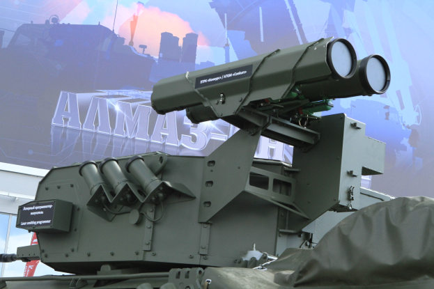 Militärfahrzeug mit einer auf einem Dach montierten Flugabwehrrakete, das vor einem Gebäude mit einer Fahne geparkt ist.