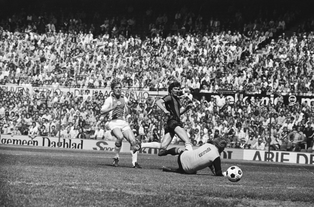 Schwarzes Foto von Männern, die auf einem Feld Füßball spielen, mit Zuschauern im Hintergrund und einer "Bundesliga 1978-79 Ajax 1-1 Hannover 96"-Fahne.