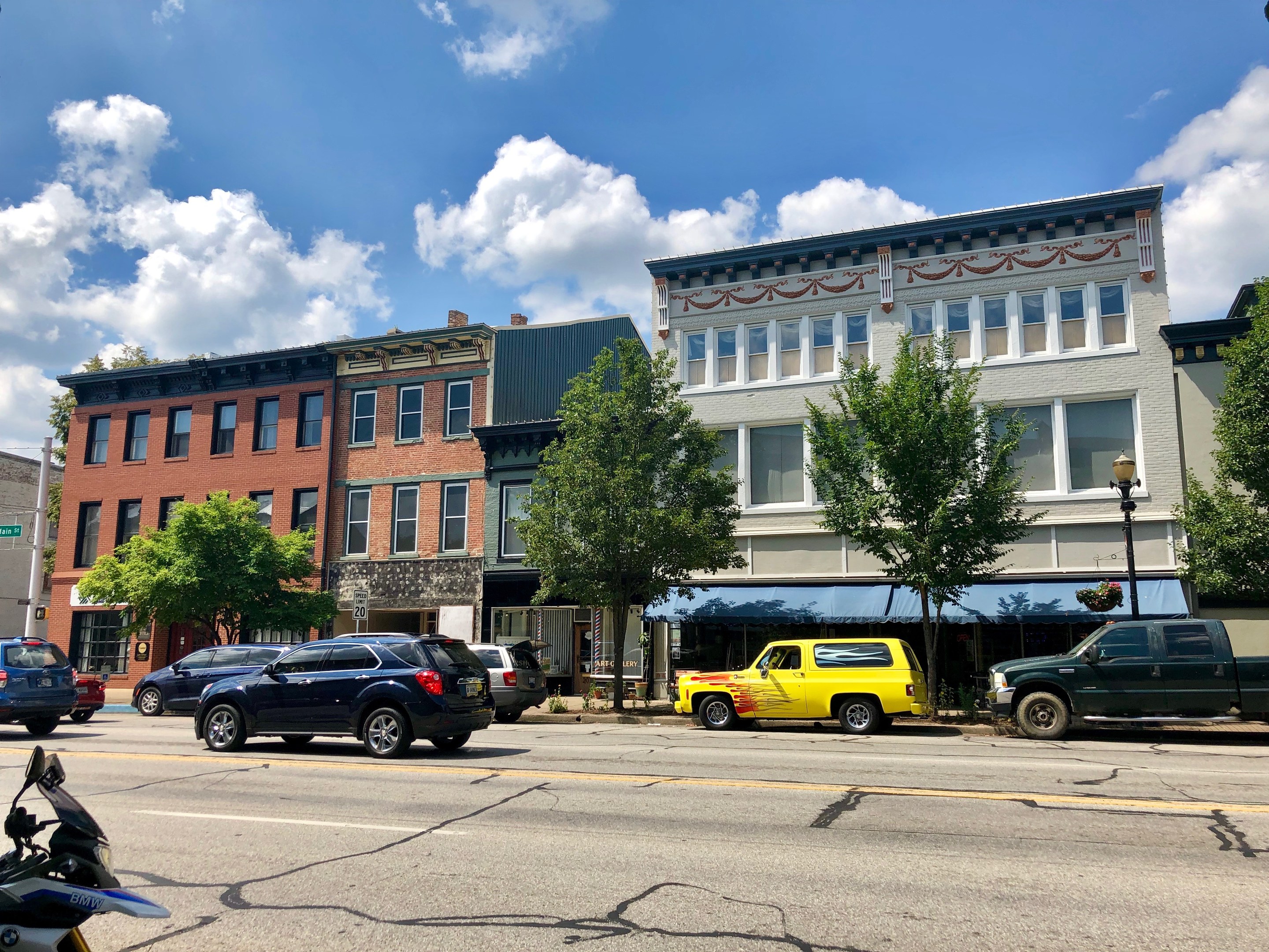 Stadtstraße mit parkenden Autos, Gebäuden, Bäumen, Laternen und einem bewölkten Himmel, mit einem Wasserzeichen "Commercial Property for Sale" zu $1,250,000.