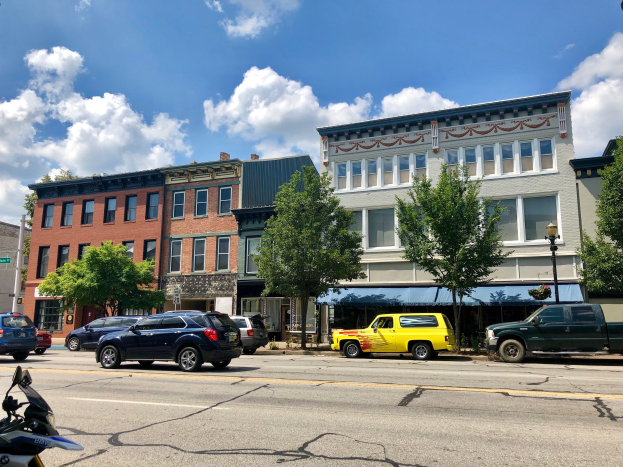 Stadtstraße mit parkenden Autos, Gebäuden, Bäumen, Laternen und einem bewölkten Himmel, mit einem Wasserzeichen "Commercial Property for Sale" zu $1,250,000.