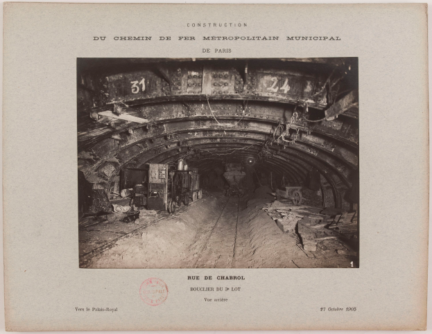 Ein altes Schwarz-Weiß-Foto eines Tunnels mit ein paar Fahrzeugen darin, das Text und einen Stempel am Boden zeigt.