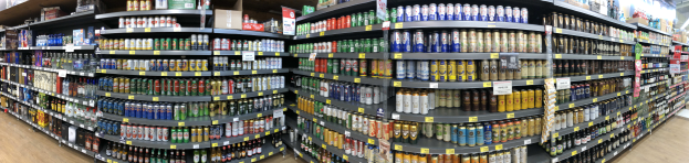 Ein Ladeneinrichtungsbild mit zahlreichen Bierflaschen in Regalen, jede mit einem Preisschild, unter heller Deckenbeleuchtung.