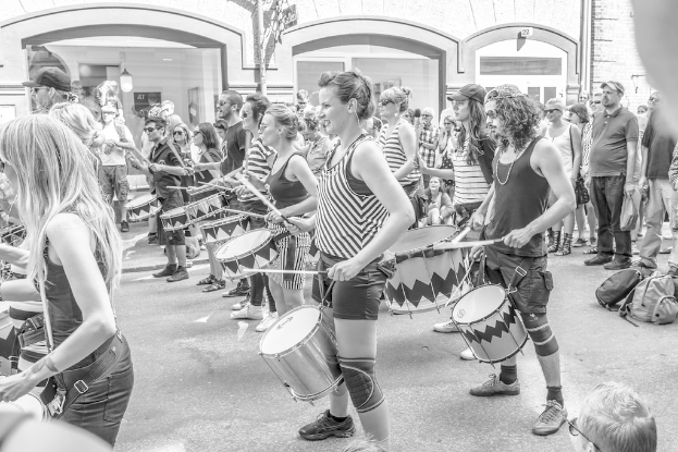 Eine Gruppe von Menschen, die draußen vor einer geschlossenen Glastür mit einer Lampe im Hintergrund Musikinstrumente spielen.