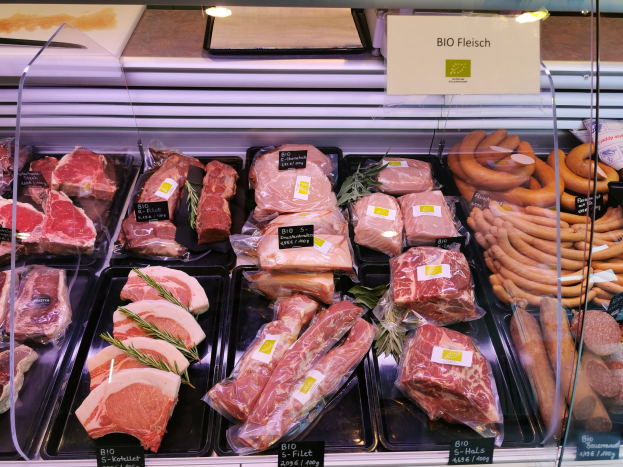 Vitrine mit verschiedenen Fleisch- und Wurstsorten in Schalen mit Preisschildern in einem Metzgerladen.