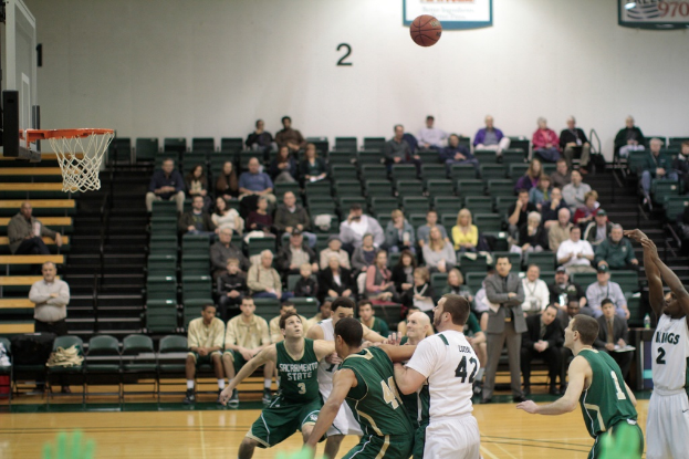 Ein Basketballfeld mit spielenden Spielern und Zuschauern auf den Tribünen im Hintergrund.