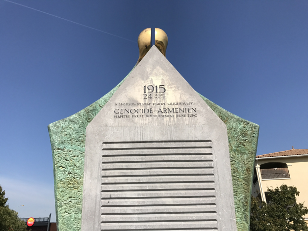 Ein hohes Denkmal mit einer Uhr darauf, umgeben von Bäumen und Gebäuden, mit einer Inschrift, die den 24. Jahrestag des Völkermords in Armenien erinnert.