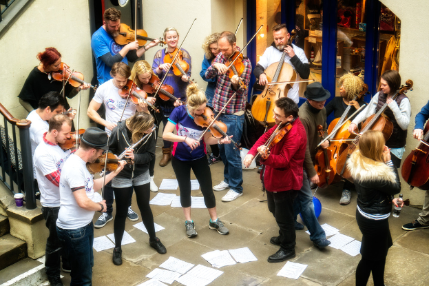 Eine Gruppe von Menschen, die Geigen spielen und Papiere auf dem Boden verstreut sind.