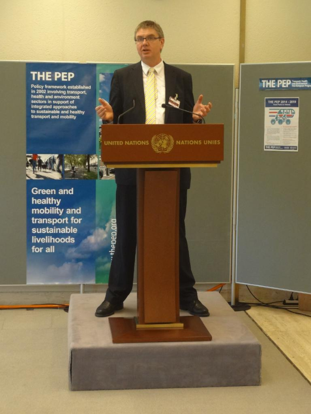 Eine Person steht an einem Podium mit einer Fahne vor einer Wand.