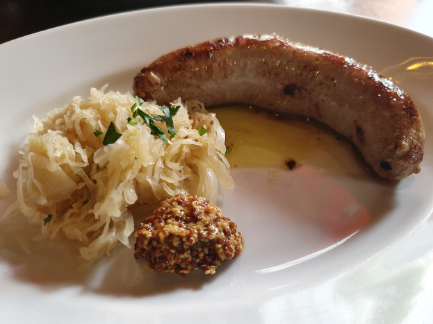Ein weißer Teller mit Sauerkraut, einer deutschen Wurst und anderen Speisen, in Nahaufnahme auf einem Tisch.