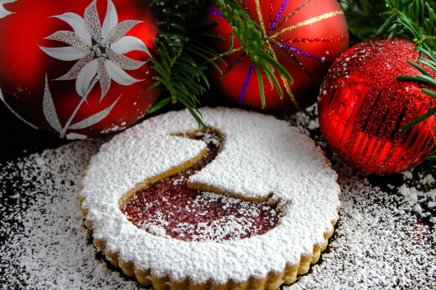 Ein Nahaufnahme eines mit Puderzucker bestäubten Weihnachtskeks mit einem herausgeschnittenen Stück, umgeben von festlichen Dekorationen wie Kugeln und Blättern.