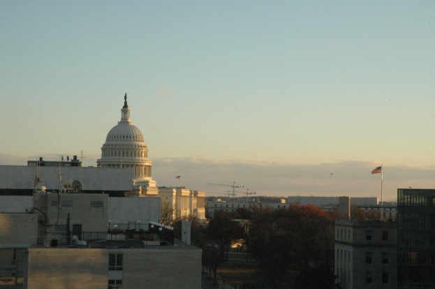 Eine Stadtansicht mit Gebäuden, Bäumen, Flaggen und einem klaren Himmel, mit einer Straße am unteren Bildrand.
