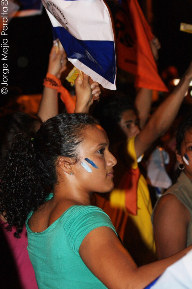 Frauen in grünen T-Shirts bei einer Demonstration, die weiße Schilder halten, mit mehreren Mädchen im Hintergrund.
