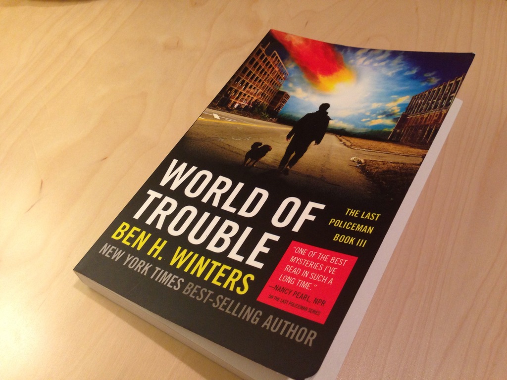 Ein Buch mit dem Titel "World Of Trouble" mit einem Bild eines Mannes und eines Hundes darauf, das auf einem Tisch liegt.