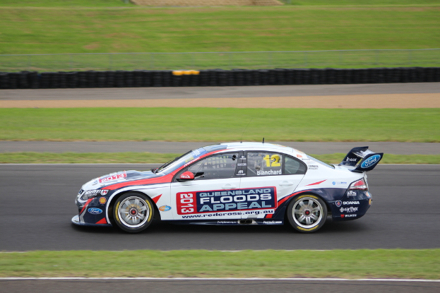 Ein Rennwagen auf einer Straße mit Gras auf beiden Seiten und vielen Reifen im Hintergrund.