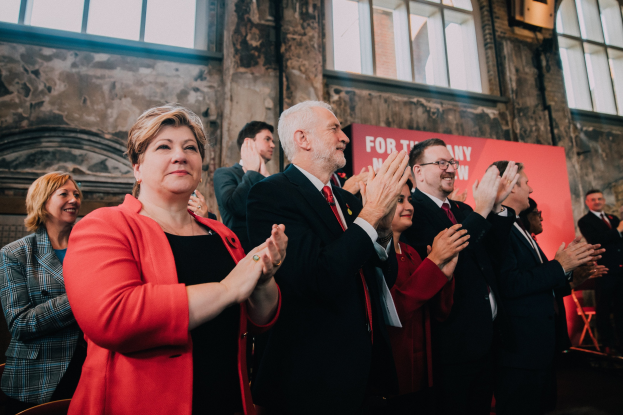 Eine Gruppe von Menschen, die vor einer Menge jubeln und ein Wahlsieg-Plakat im Hintergrund halten.