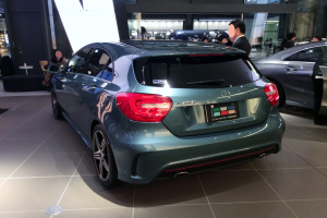 Ein Mercedes-Benz A-Klasse Hatchback auf der IAA in Frankfurt, ein schlankes, modernes Design mit glänzender schwarzer Lackierung, Chromakzente, sportliches Aussehen, niedriger Profil, breite Basis, markantes Grill und Aluminiumräder, umgeben von einer Gruppe von Menschen.