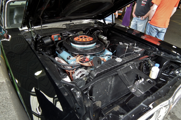 Nahaufnahme von Autokühlerteilen mit unscharfen Personen und einer Straße im Hintergrund.