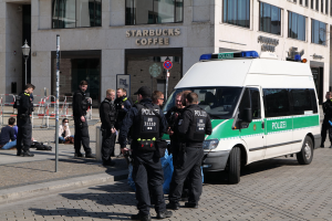 Eine Gruppe von Polizisten steht vor einem Starbucks-Kaffeehaus, mit einem Van auf der rechten Seite und einigen Menschen auf der linken Seite; ein Gebäude, ein Schild, ein Laternenpfahl und ein Zaun sind im Hintergrund zu sehen.