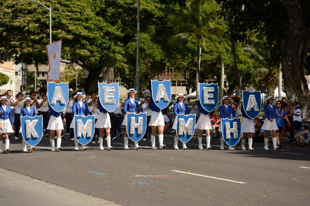 Schülerinnen mit Buchstabenkarte gehen auf einer Straße mit Bäumen im Hintergrund.