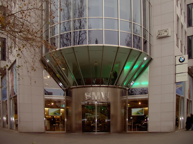 Großes BMW-Hauptquartier-Gebäude in Frankfurt mit Glasfront und Text an der Fassade, Menschen vor dem Gebäude und einem Baum links.
