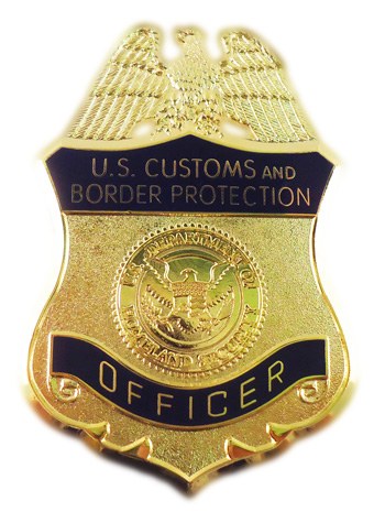 Goldabzeichen mit der Aufschrift "U.S. Customs and Border Protection Officer" vor einem weißen Hintergrund.