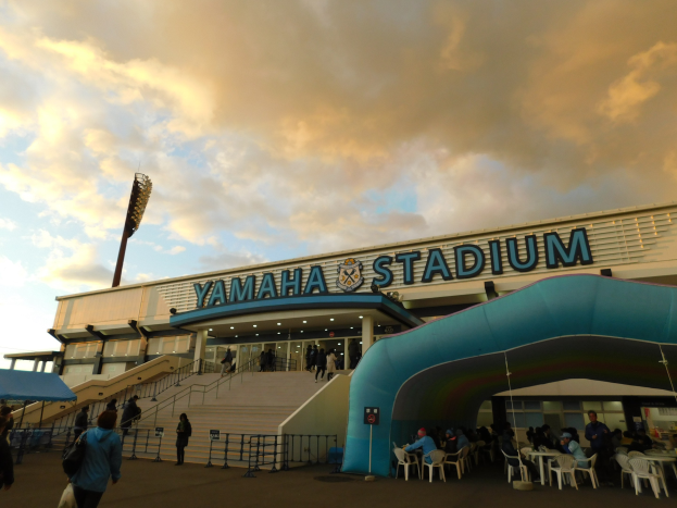 Yamaha-Stadion in San Francisco mit Menschen auf Sitzen und Stehen in der Nähe des Eingangs, Geländern, Stufen, einem Zelt auf der linken Seite und einem bewölkten Himmel im Hintergrund.