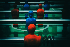 Ein buntes Tischfußballtisch mit einer Gruppe von Menschen in verschiedenenfarbigen Trikots, positioniert in der Mitte des Tisches, bereit für ein Spiel von Tischfußball.