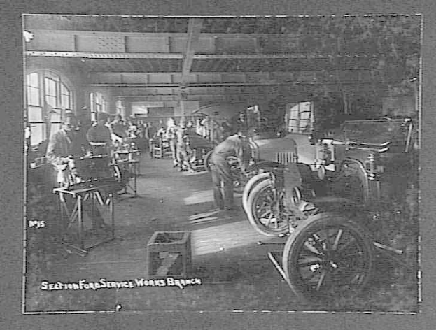 Schwarzes und weißes Foto von Männern, die an Autos in einer Ford-Servicewerkstatt arbeiten, mit Fahrzeugen, Werkzeugen und Fenstern.