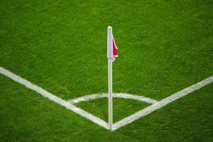 Ein Fußballfeld mit grünem Gras, weißen Begrenzungslinien und einem weißen Pfosten mit einer roten und weißen Flagge in der Mitte des Elfmeterpunkts.