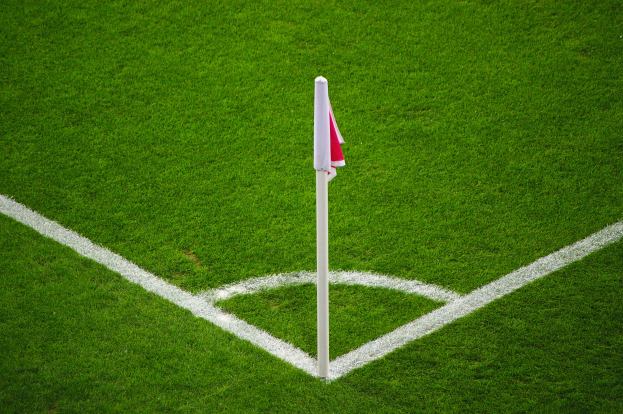 Ein Fußballfeld mit grünem Gras, weißen Begrenzungslinien und einem weißen Pfosten mit einer roten und weißen Flagge in der Mitte des Elfmeterpunkts.