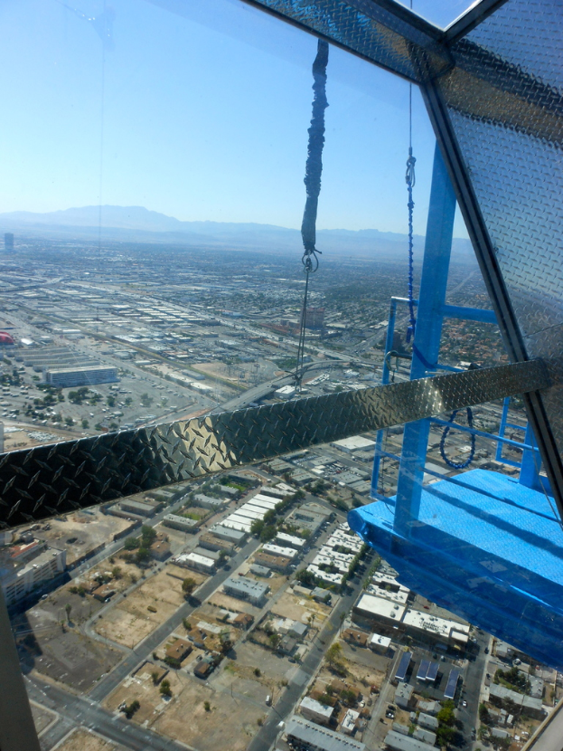 Luftaufnahme einer Stadt mit Häusern und Bäumen, eine Fußgängerbrücke auf der linken Seite, Hügel im Hintergrund und einen klaren Himmel darüber.