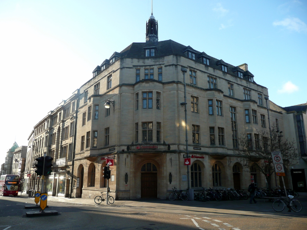 Ein Gebäude mit Fenstern und Türen in der Mitte, ein Bus auf der linken Seite, Fahrräder unten, ein Baum auf der rechten Seite und Himmel oben.