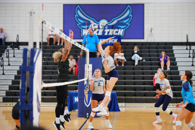 Frauen beim Volleyballspielen mit Netz, Zuschauern auf Treppe und einem Banner zum Sieg in der Staatsmeisterschaft.