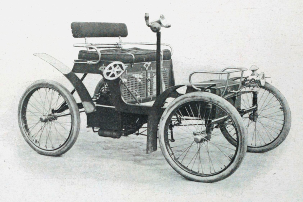 Ein Schwarz-Weiß-Foto eines frühen 1900er-Elektroautos mit schlankem, aerodynamischem Design, großem runden Scheinwerfer, gewölbter Dachlinie, vier großen Rädern, einem prominenten Heckmotor, hellfarbiger Polsterung und einem Armaturenbrett mit Knöpfen und Drehreglern.